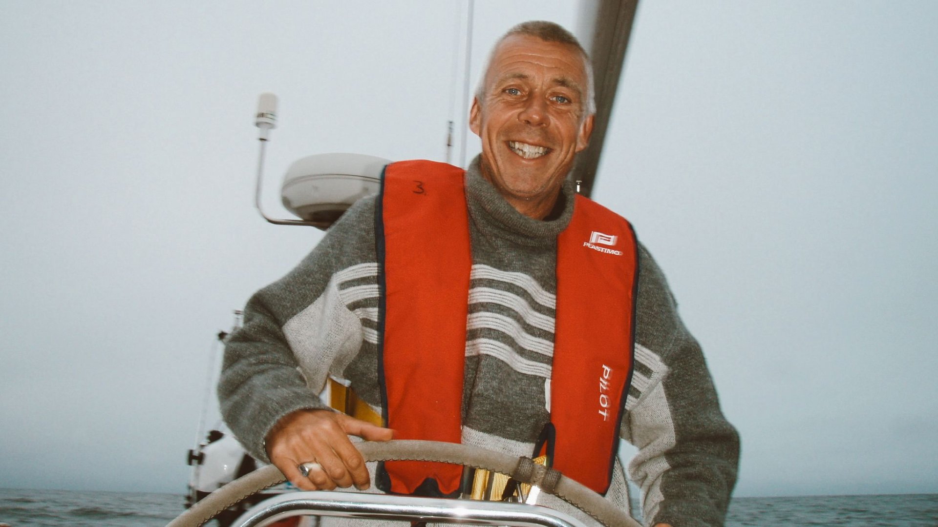 Smiling skipper in an orange life vest at the helm of a yacht