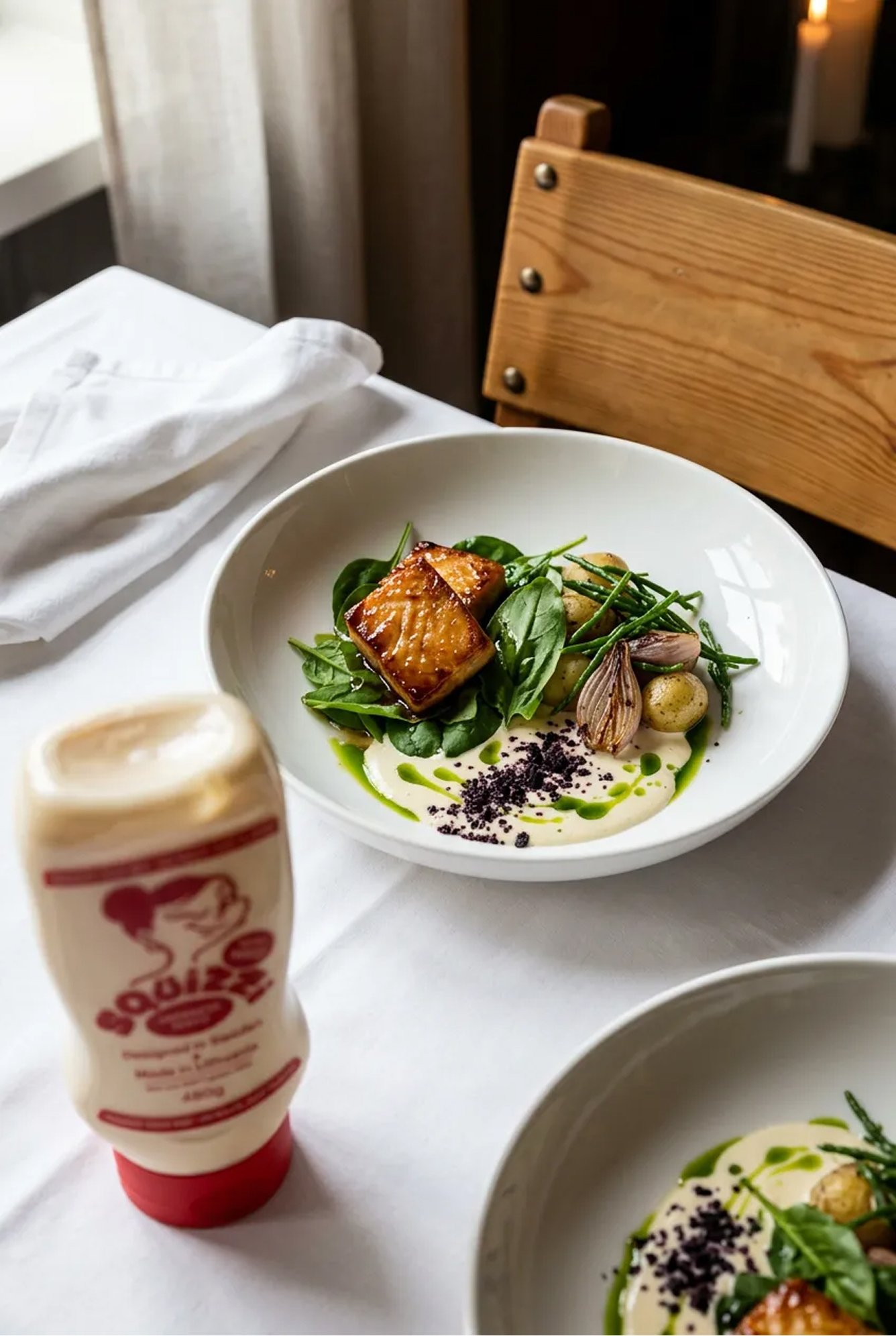 Plated salmon dish on a laid table beside a Squizzi mayo bottle